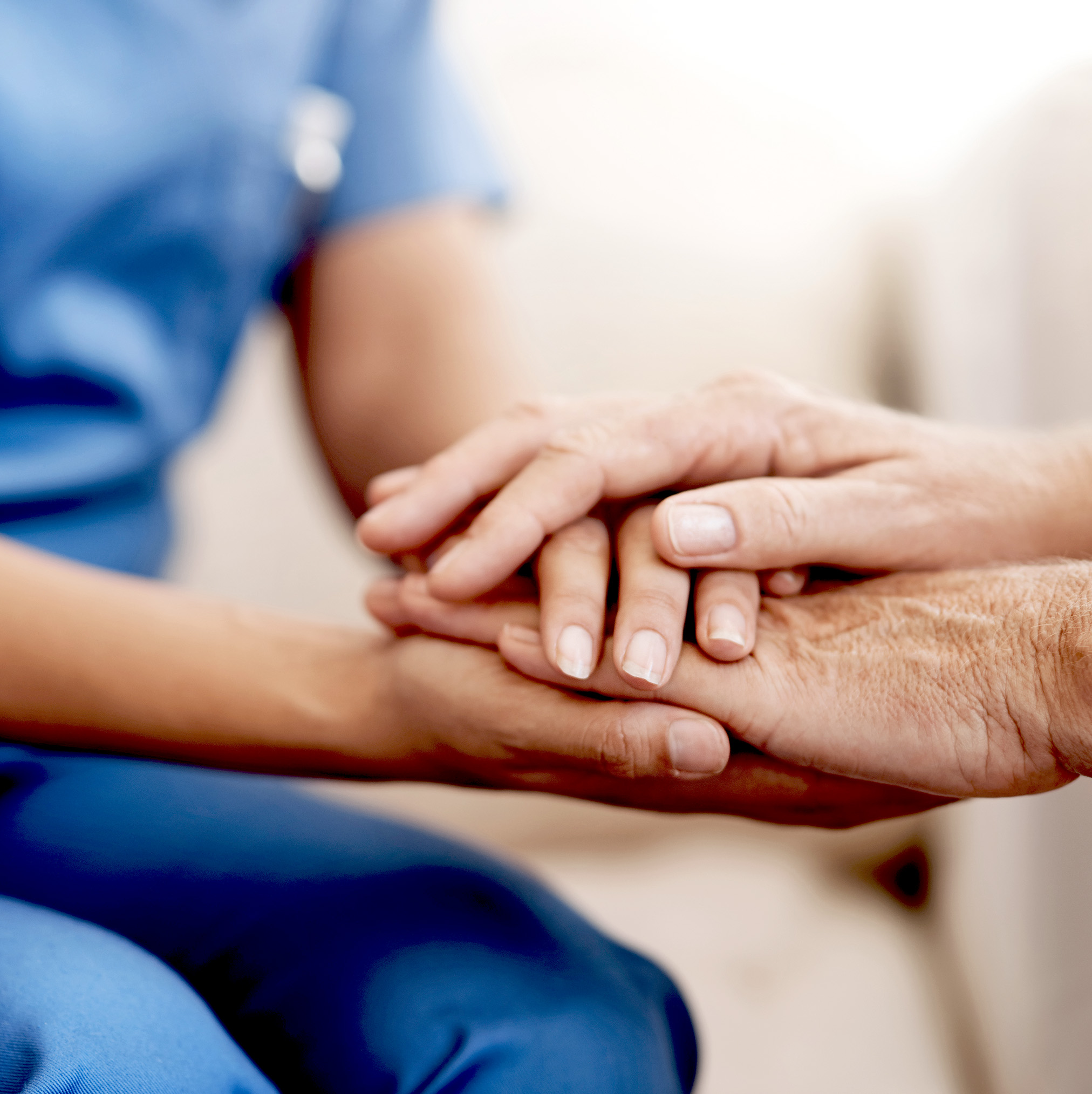 Eine Pflegerin legt tröstend ihre Hände auf die Hände eines Patienten.